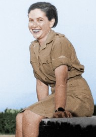 Eine junge Frau in Militäruniform sitzt lächelnd im Freien auf einem Steinsockel