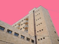 Ein hohes Gebäude im Bauhaus-Stil mit kleinen Fenstern vor einem pinken Bildhintergrund