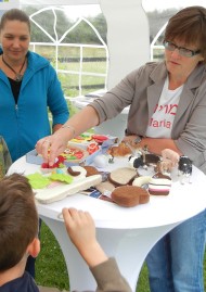 Eine Führungsmitarbeiterin erklärt mihilfe von Spielzeug einem Jungen und einer Frau religiöse Nahrungsvorschriften